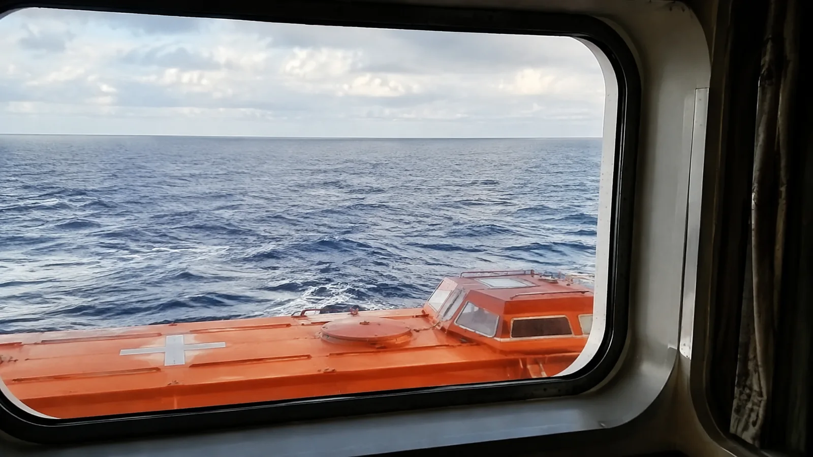 Orange lifeboat roof partly blocks the lower stateroom window view.