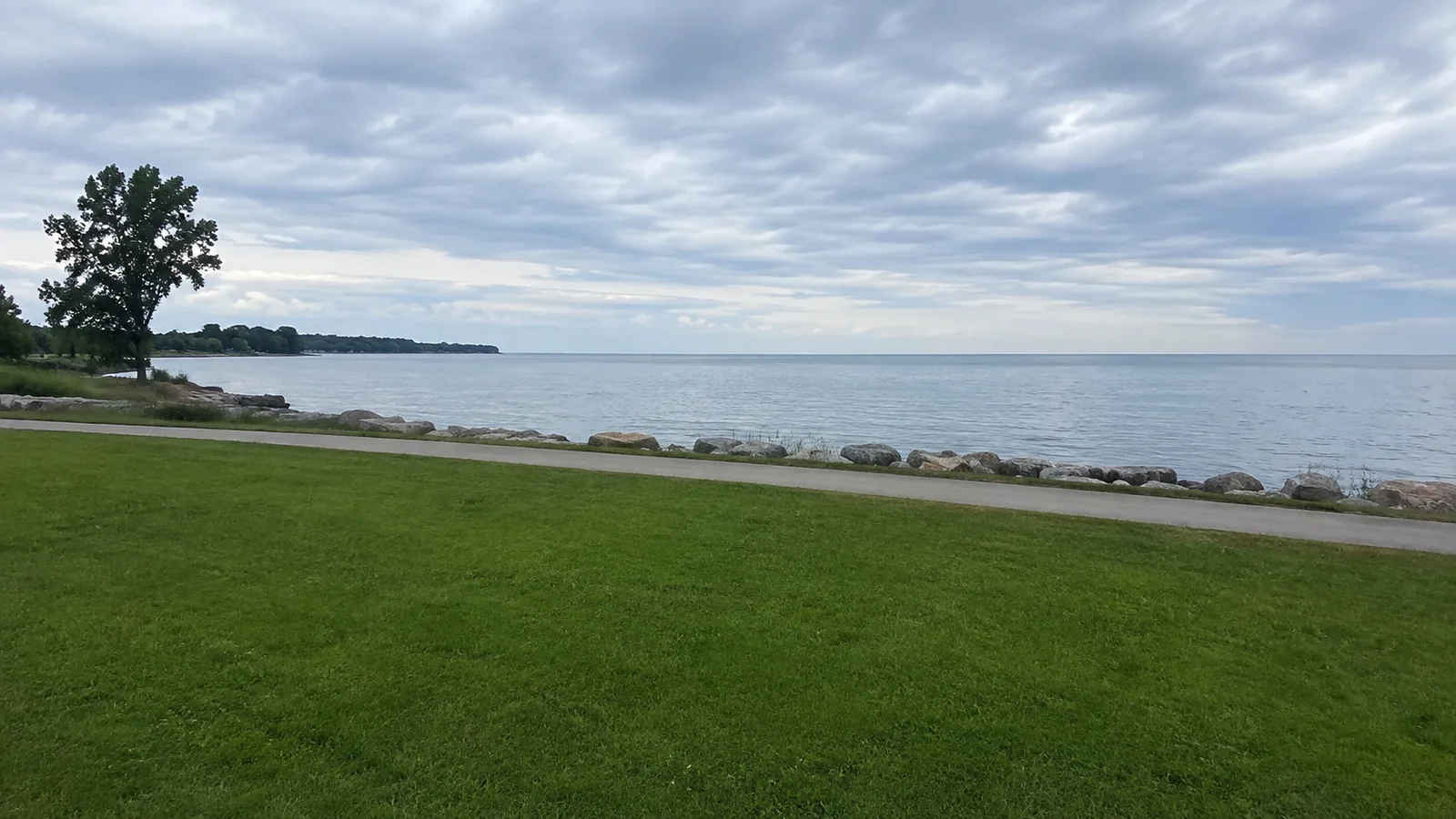 Grassy waterfront park beside a calm lake beneath layered clouds.