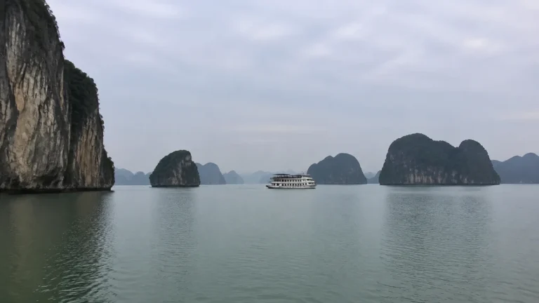 Cruise boat sailing among steep rocky islands beneath an overcast sky.