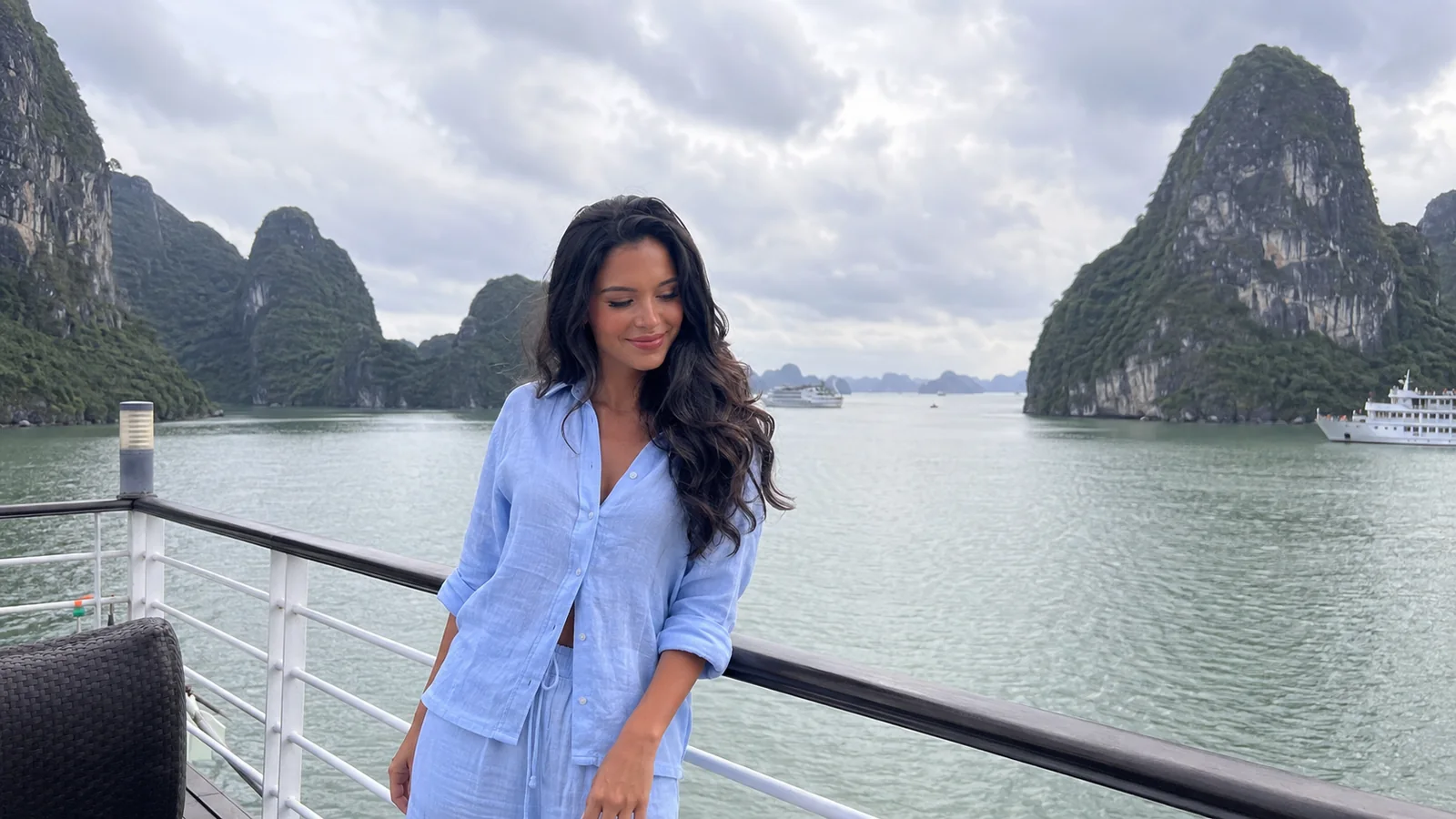 Woman in a blue shirt standing by a boat railing with limestone islands behind her.