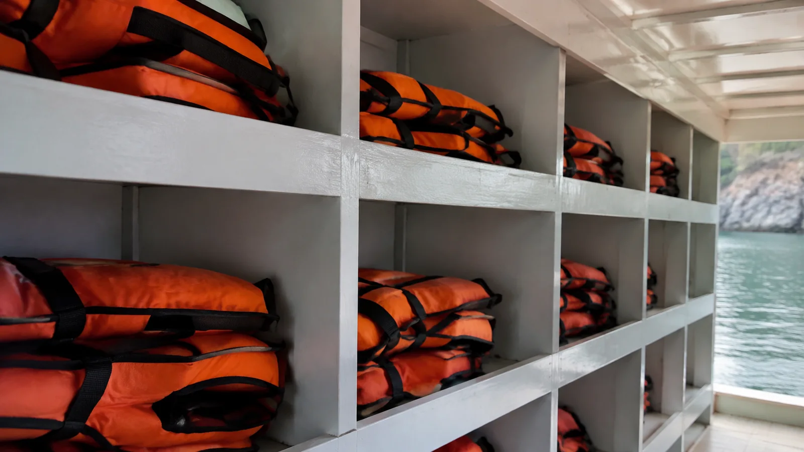 Orange life jackets stacked inside white storage cubbies on a boat.