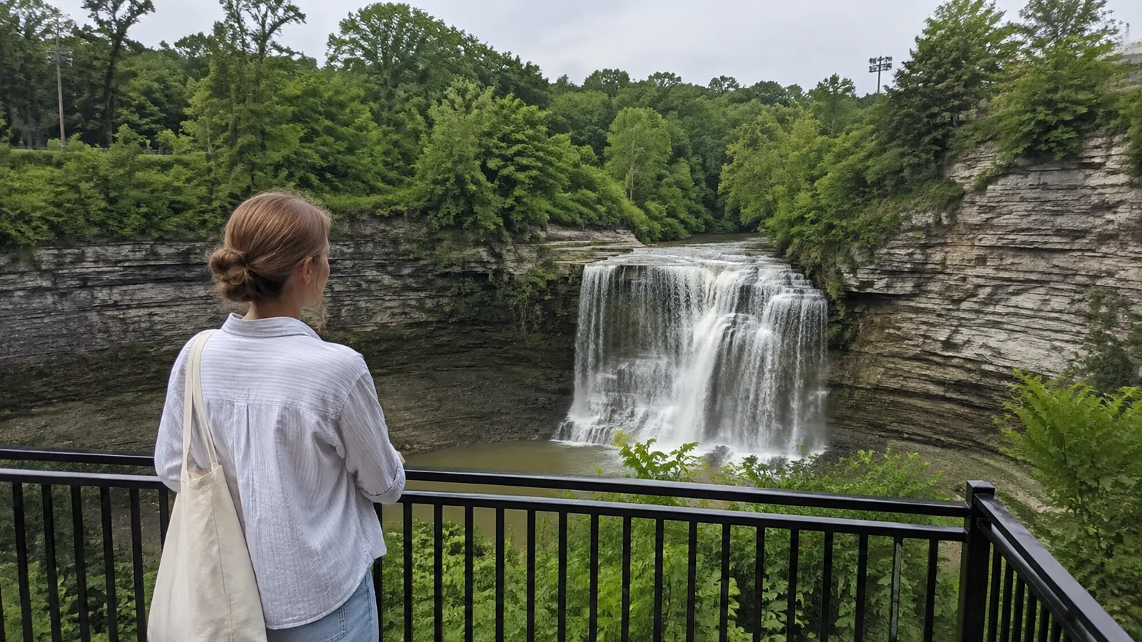 Visitor watches a waterfall cascade over layered rock into a gorge.