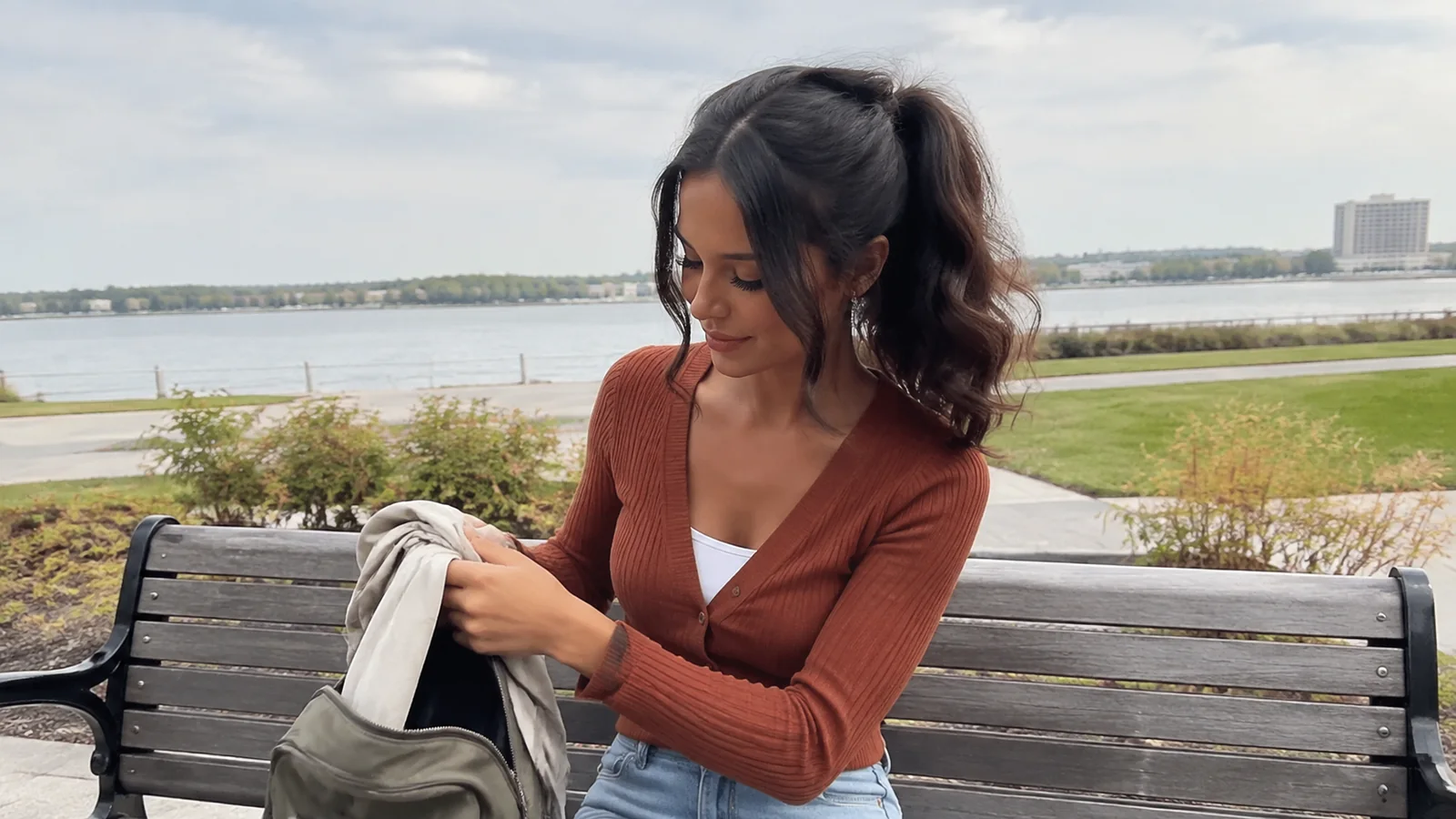 Woman packs a light garment into a bag on a lakeside bench.