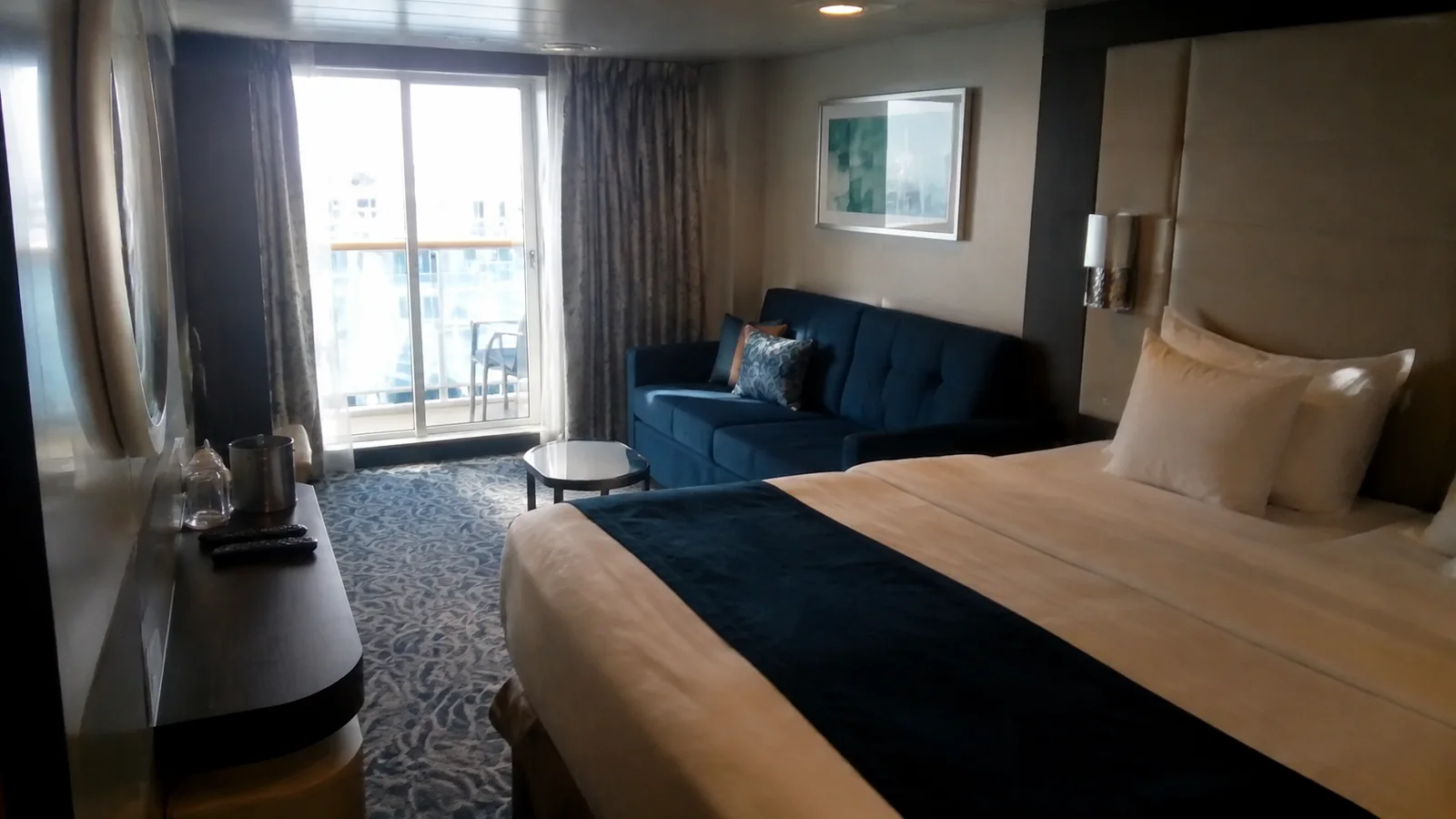 Cruise cabin with a double bed, blue sofa and balcony doors.