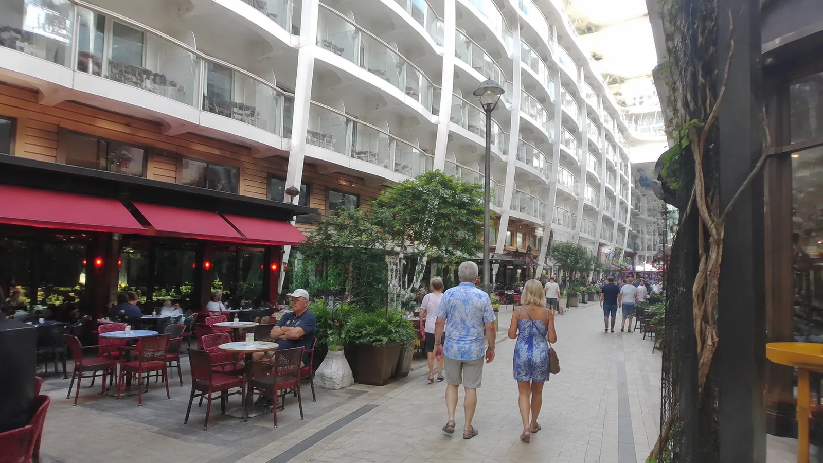 Passengers walking through an open-air ship courtyard lined with balconies and cafes.
