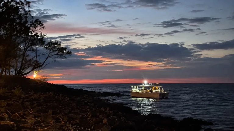 Illuminated dive boat sits offshore beneath a colorful sunset sky.