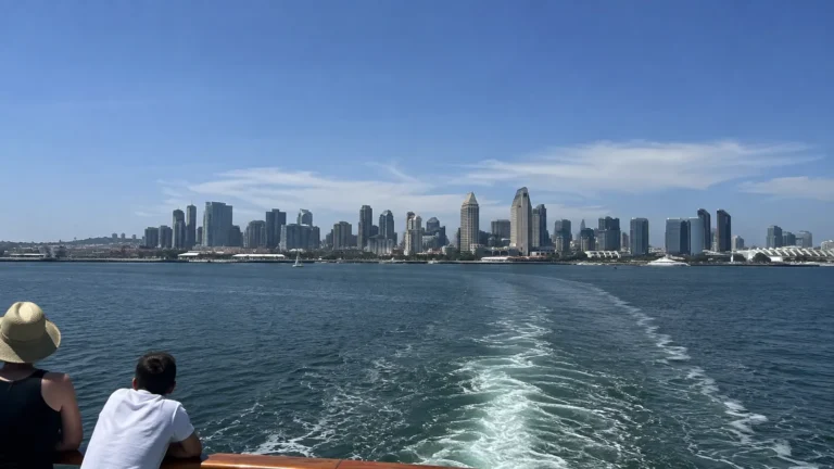 Ship's wake stretching toward a distant city skyline