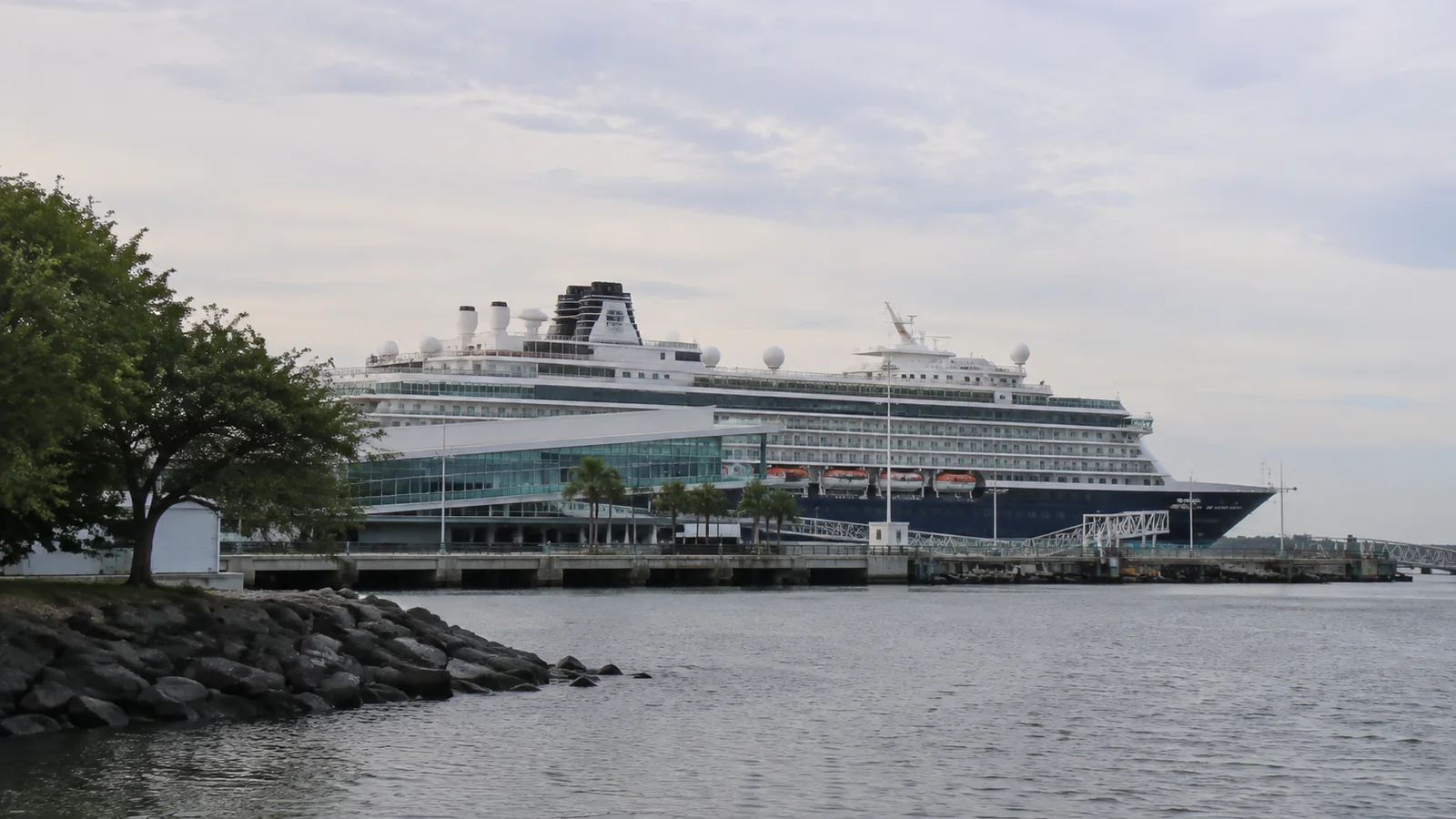 Cruise ship docked beside a waterfront terminal under an overcast sky.