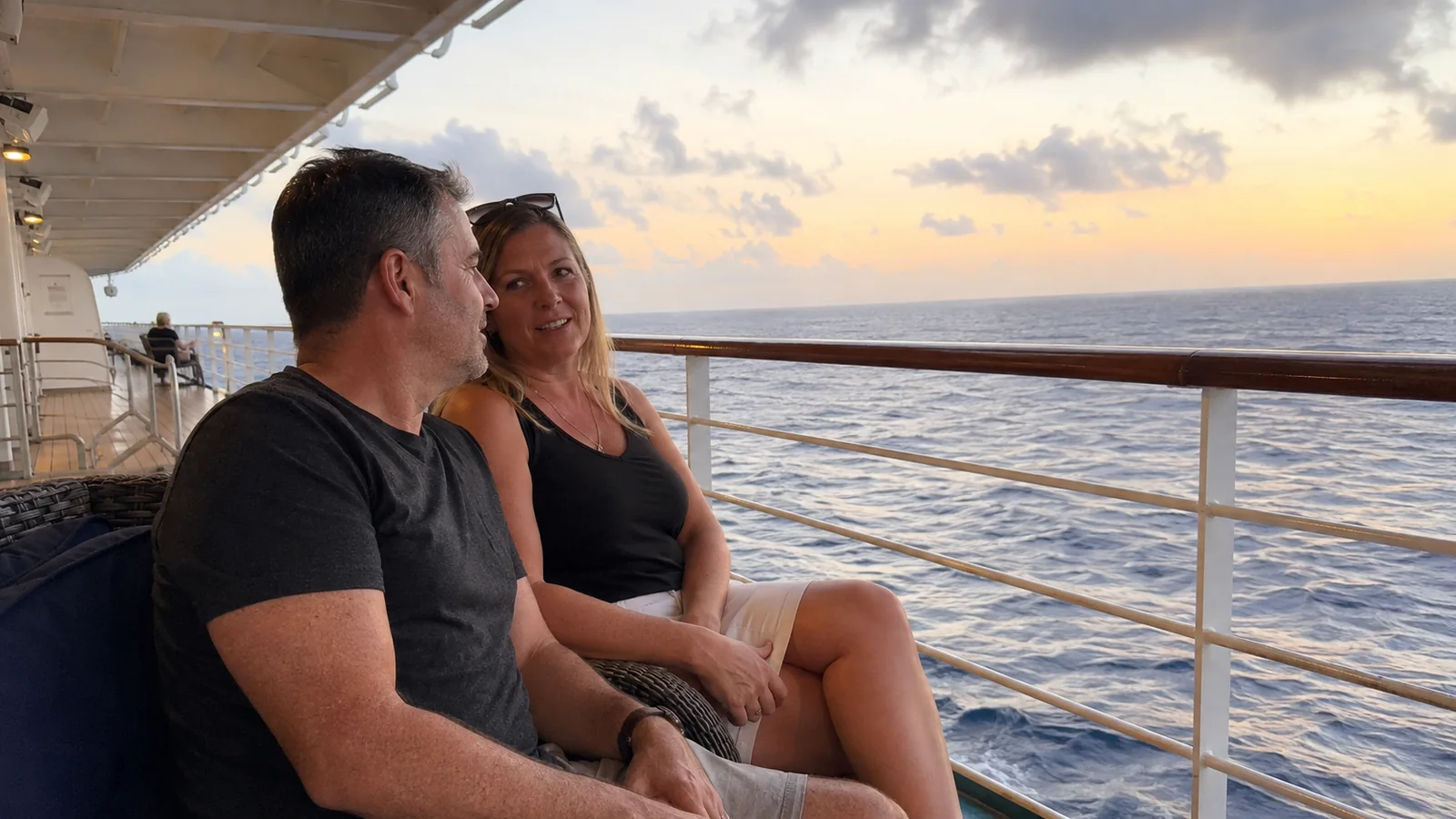Couple sitting together on an outside ship deck at sunset.