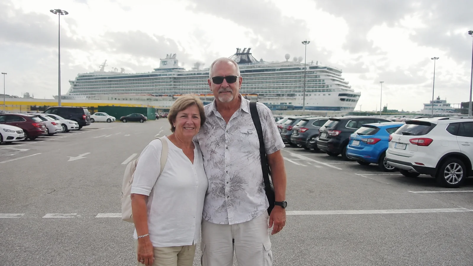 Couple stands in a parking lot with a cruise ship behind them.