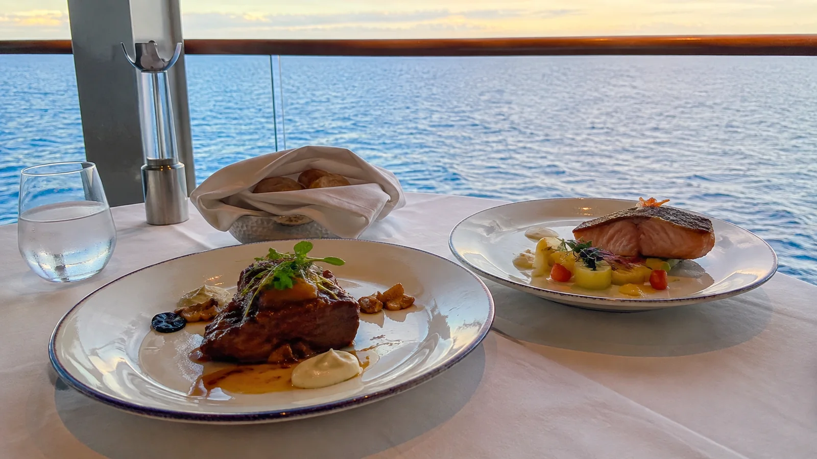 Two plated meals sit on a table beside an ocean window.