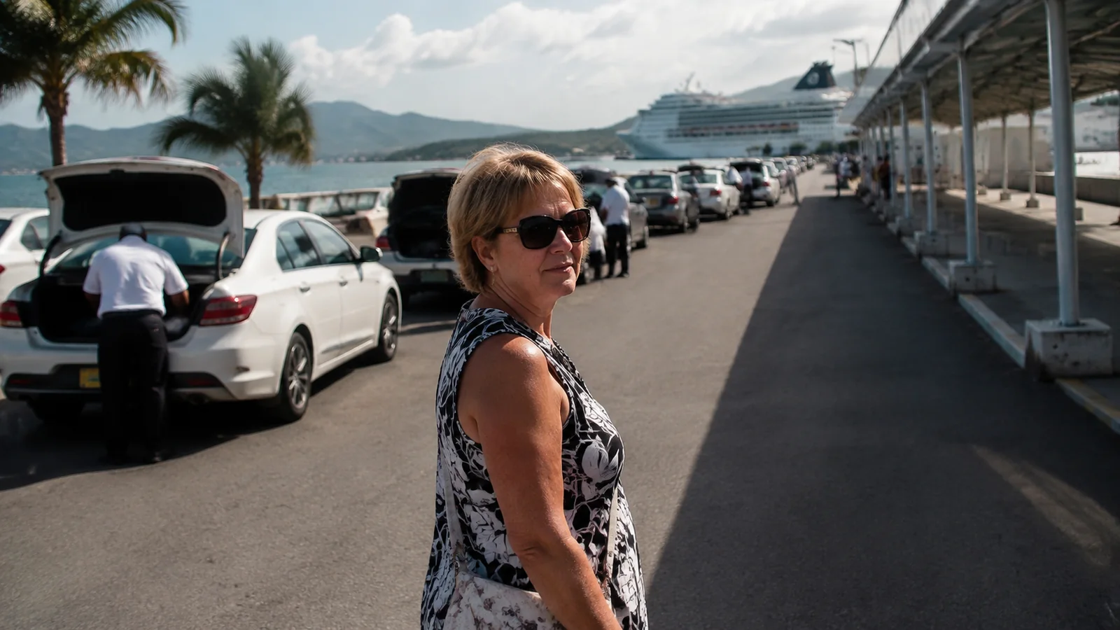 Woman stands beside parked cars near a cruise terminal.