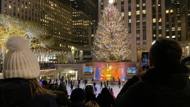 Visitors watching a large illuminated Christmas tree above an ice rink.