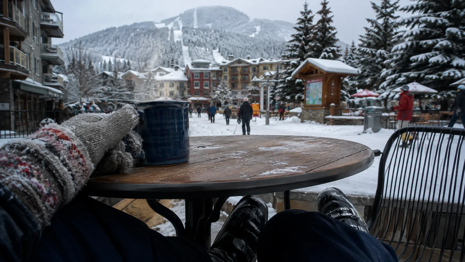 Gloves and a warm drink on a table overlooking a snowy resort village.