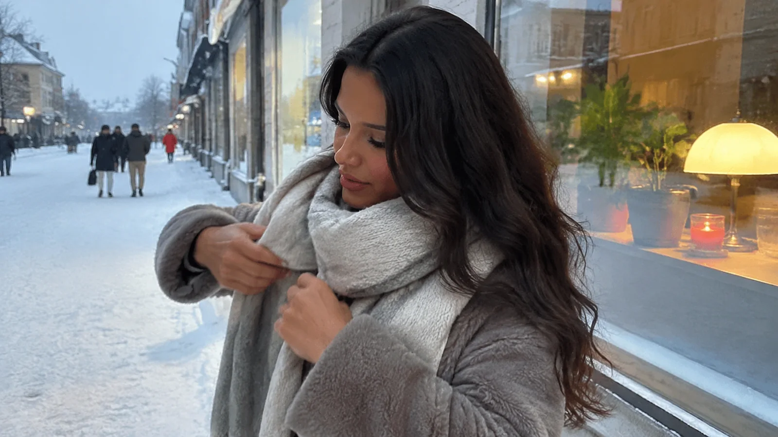 Woman adjusting a scarf on a snowy shopping street.