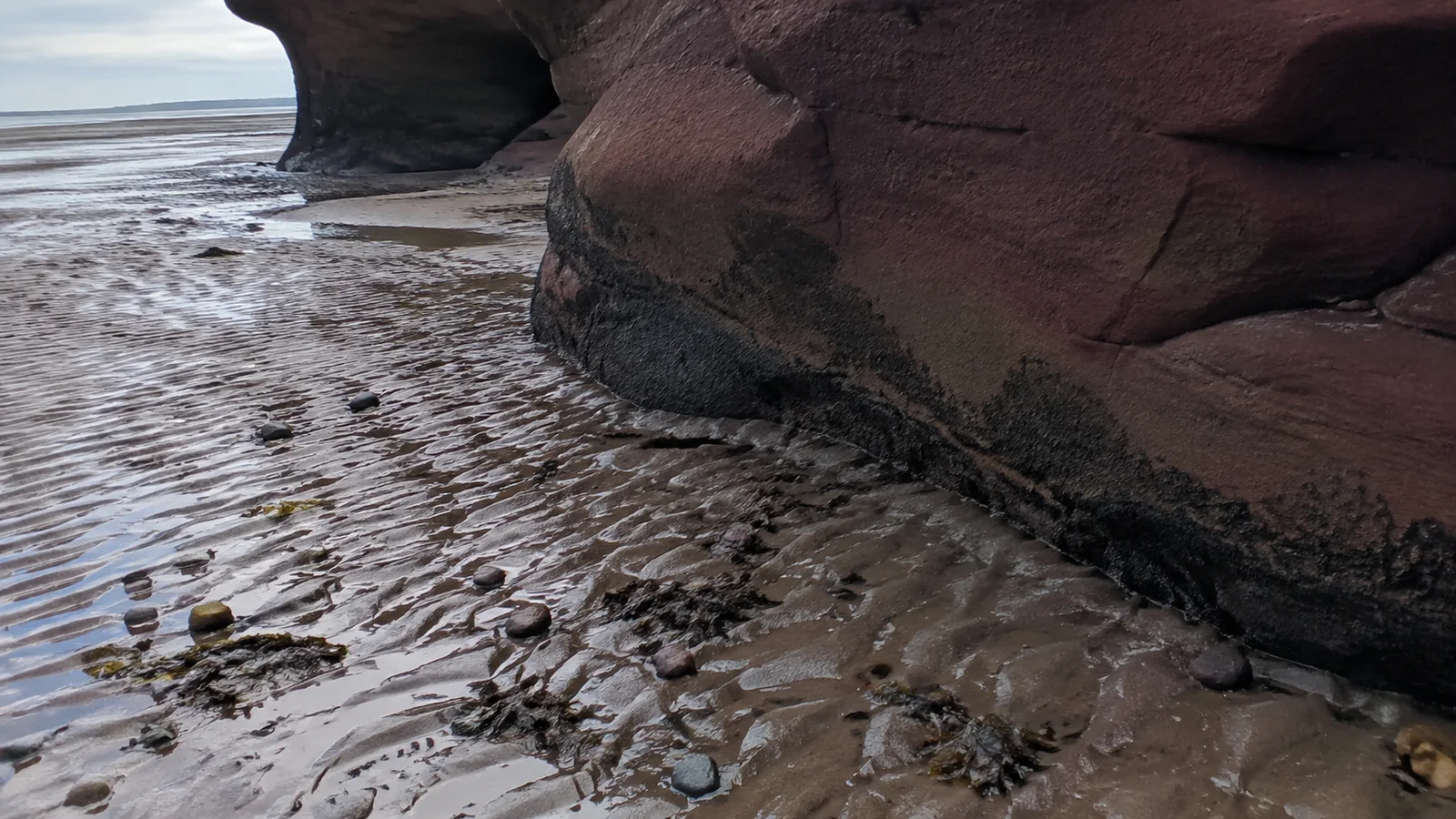 Ripples in wet sand beside the base of a reddish sea stack.