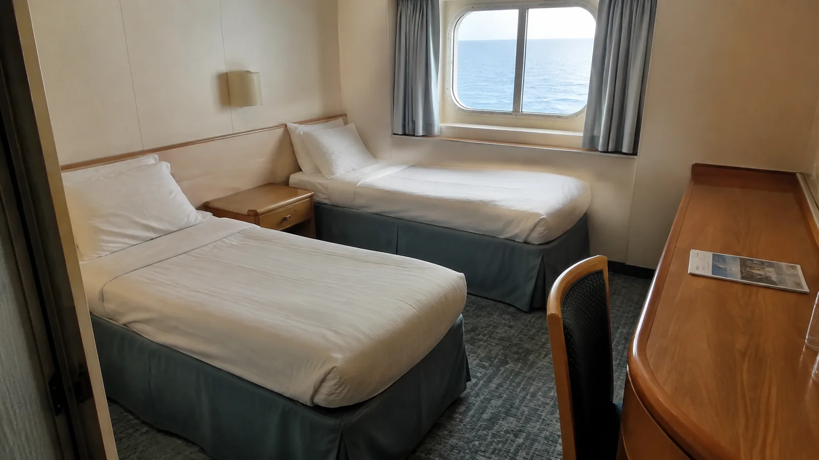 Compact stateroom contains twin beds, a desk and an ocean window.