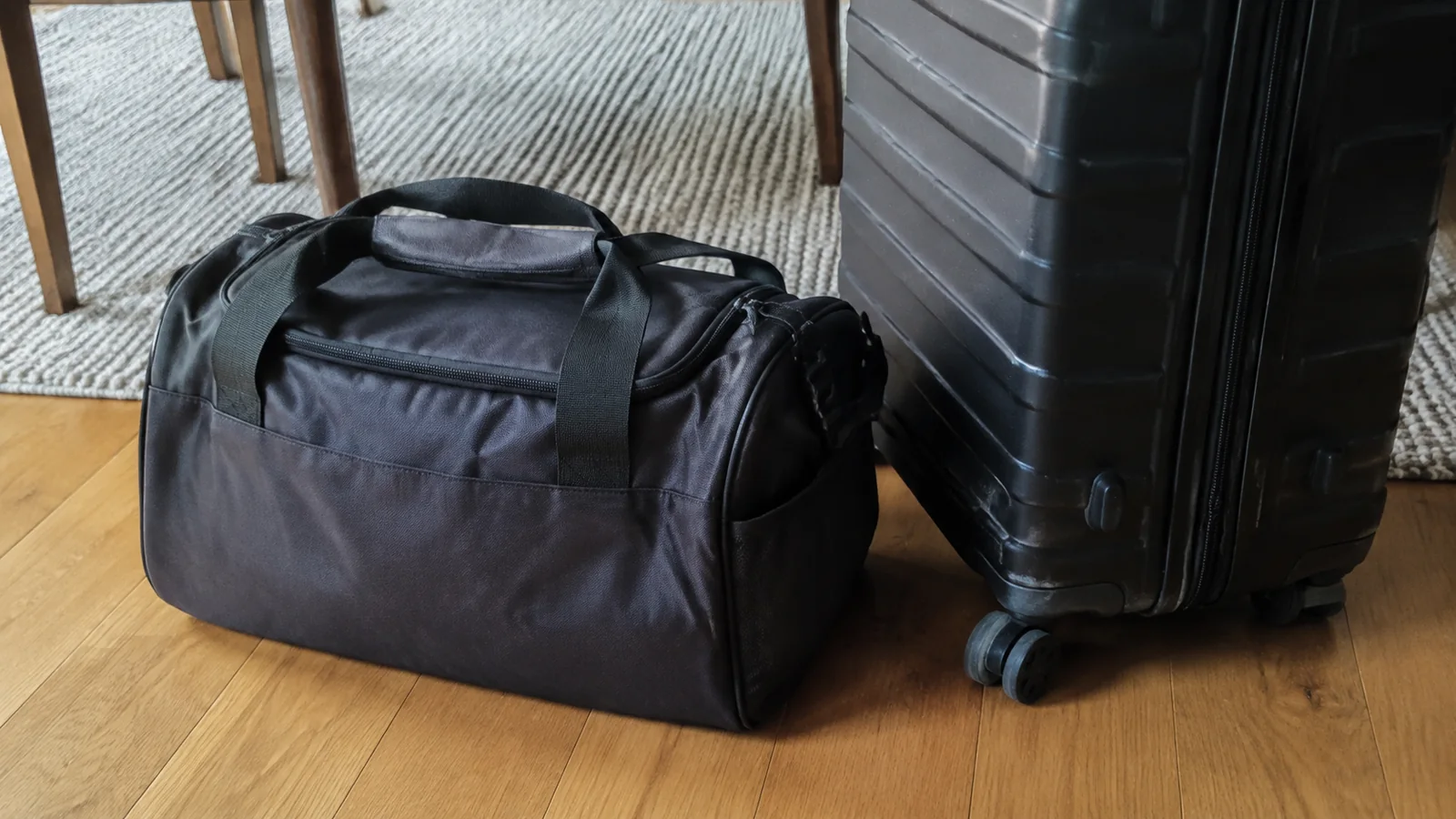 Small duffel bag beside a large hard-shell suitcase.
