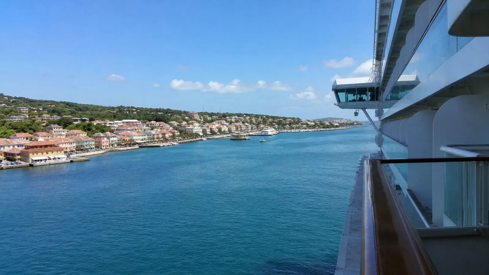 Coastal town seen from a cruise ship balcony above blue water.