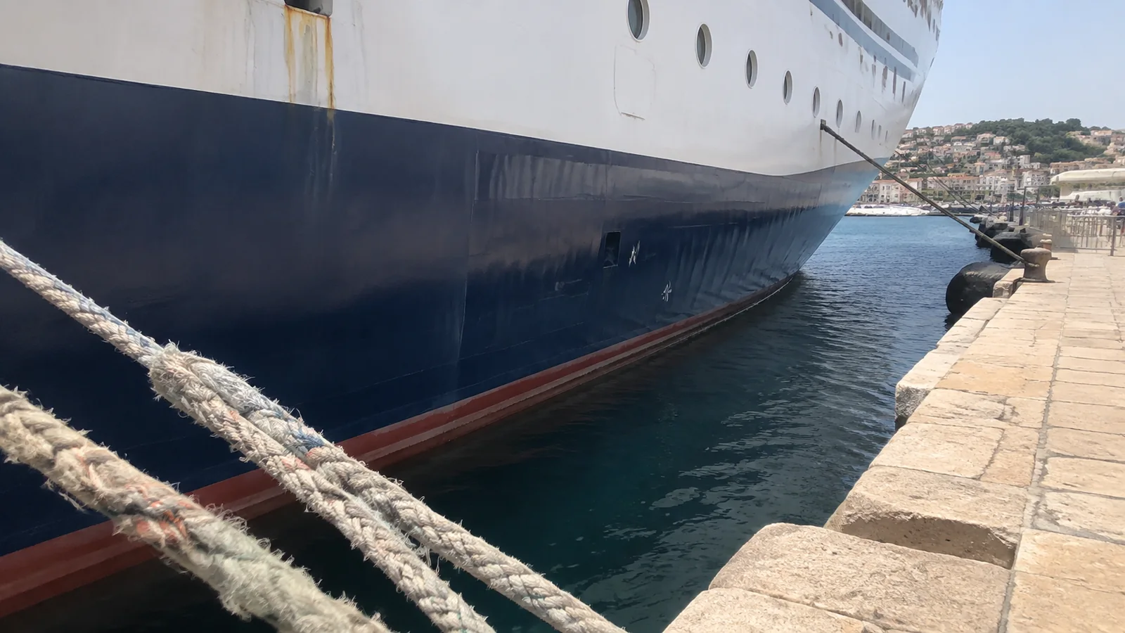 Thick mooring ropes securing a ship's hull to a stone quay.