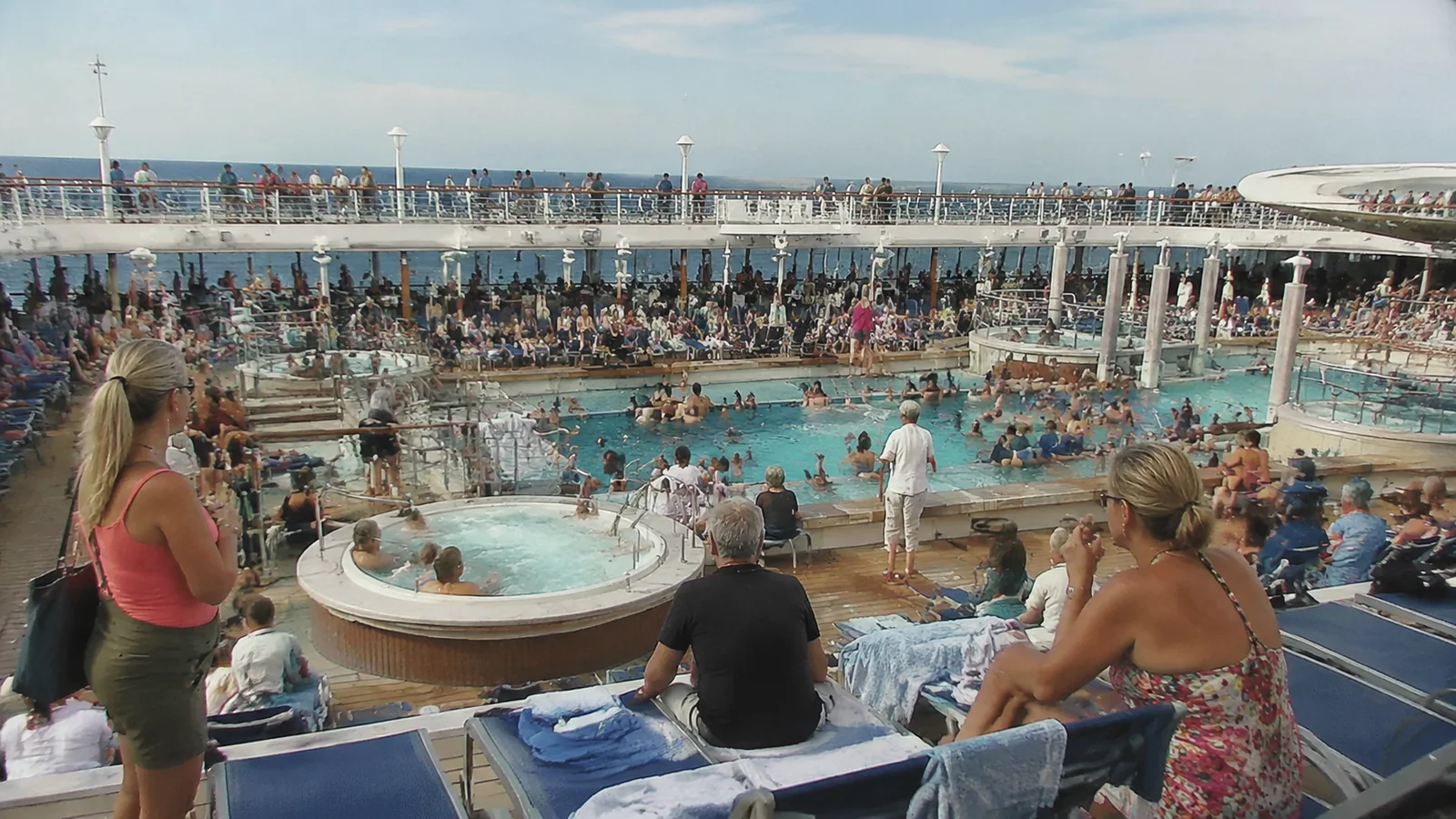 Crowded cruise ship pool deck with hot tubs