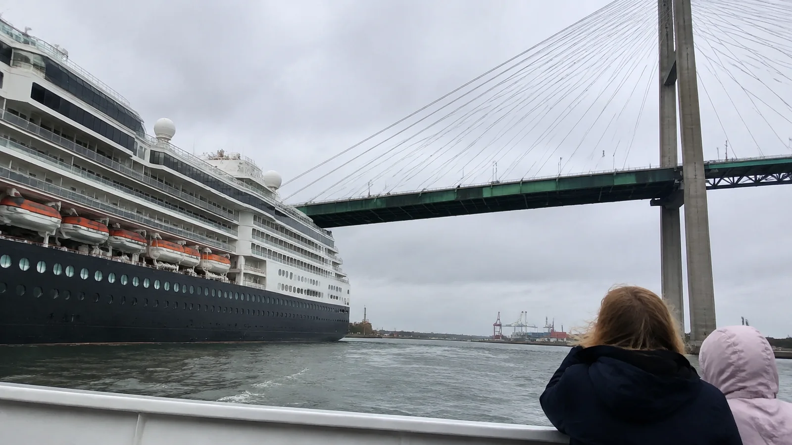 Cruise ship passing beneath a bridge while passengers watch