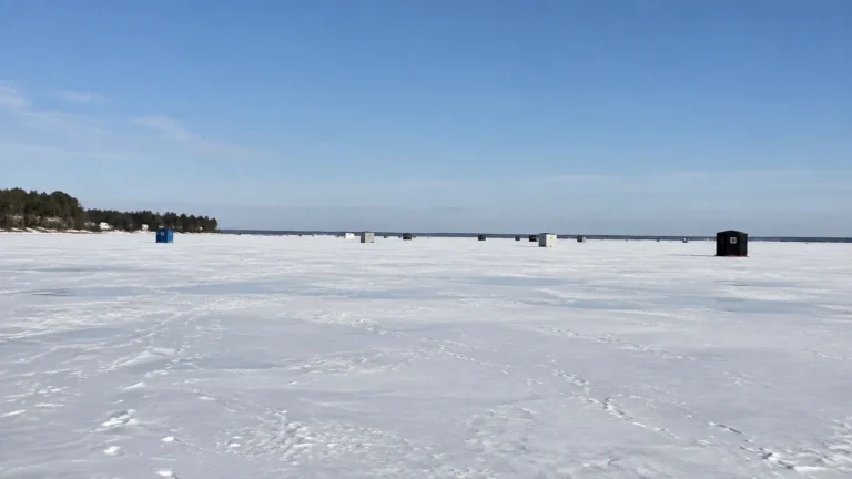 Ice fishing shelters scattered across a vast snow-covered frozen lake.