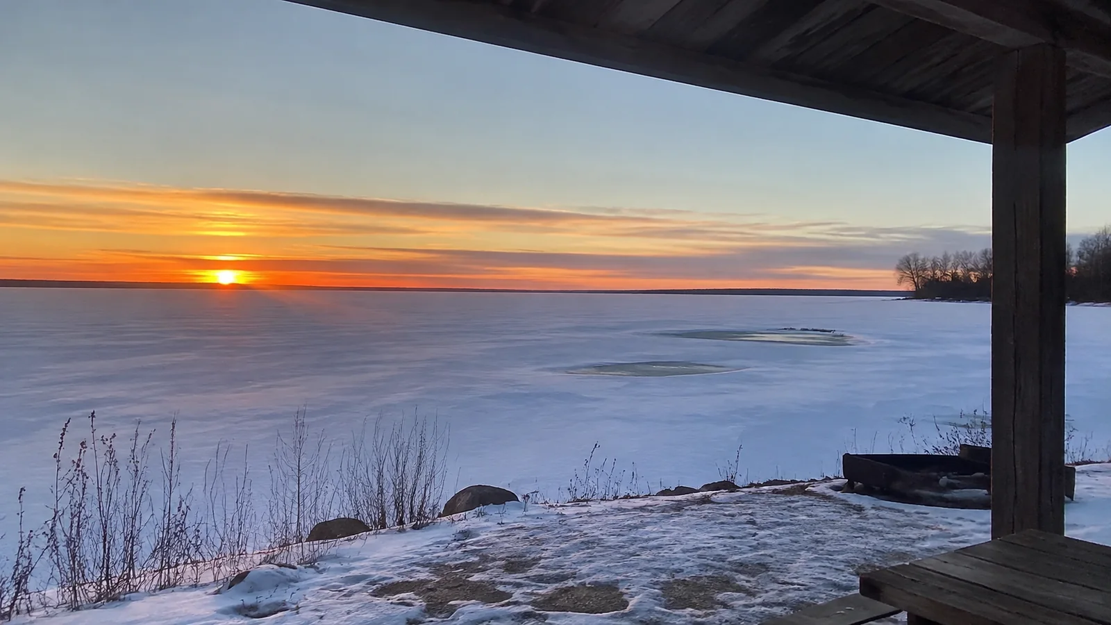 Orange sunset over a frozen lake viewed from a sheltered porch.