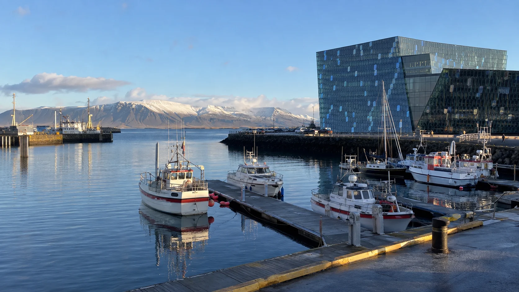 Fishing boats, Harpa Concert Hall, and mountains across Reykjavík's Old Harbor.