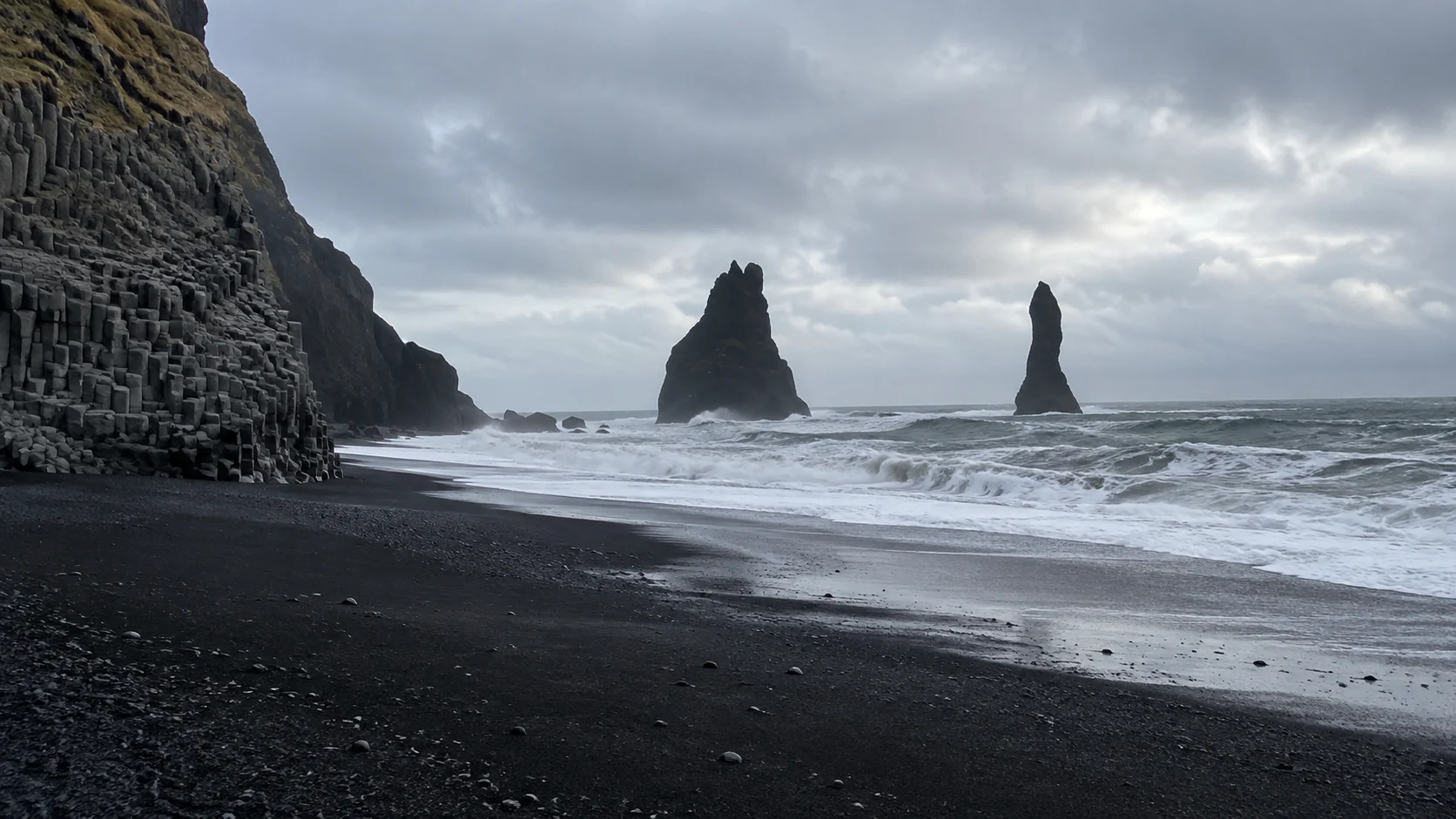 Basalt sea stacks and Atlantic waves along Reynisfjara black-sand beach.