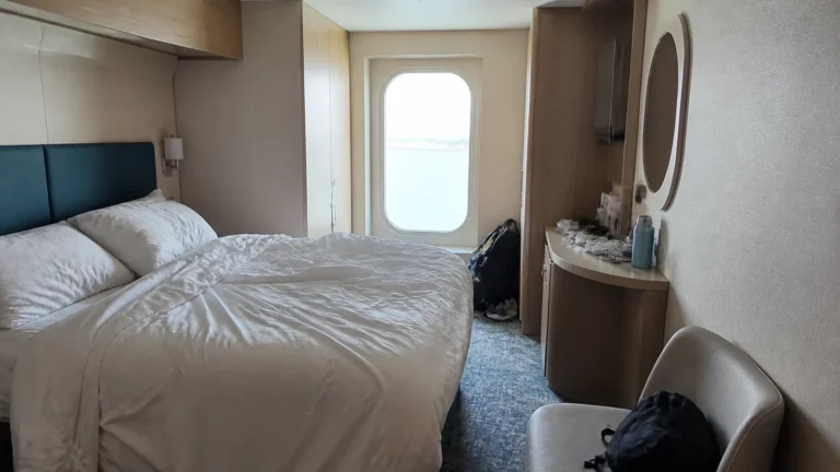 Modern cruise cabin with a double bed, desk, and narrow window