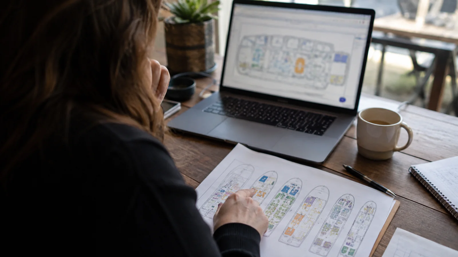 Woman comparing printed deck plans with a cruise ship layout on a laptop