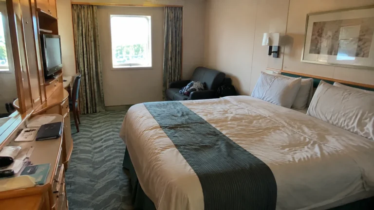 Cruise cabin with a double bed, wooden desk, and window