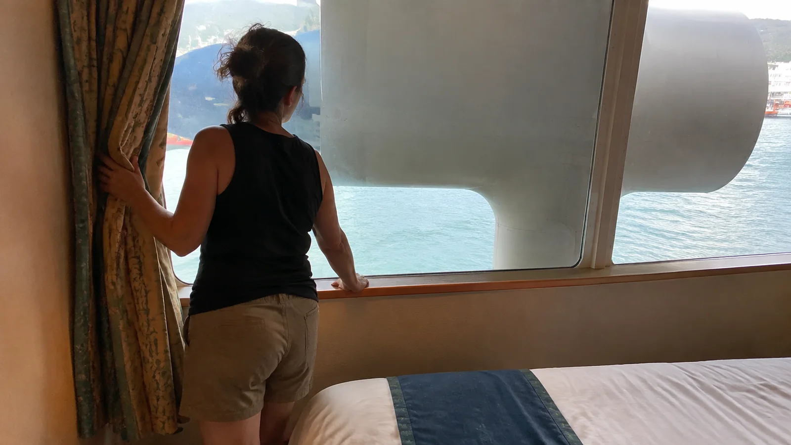 Woman looking through a cruise cabin window partly blocked by ship equipment