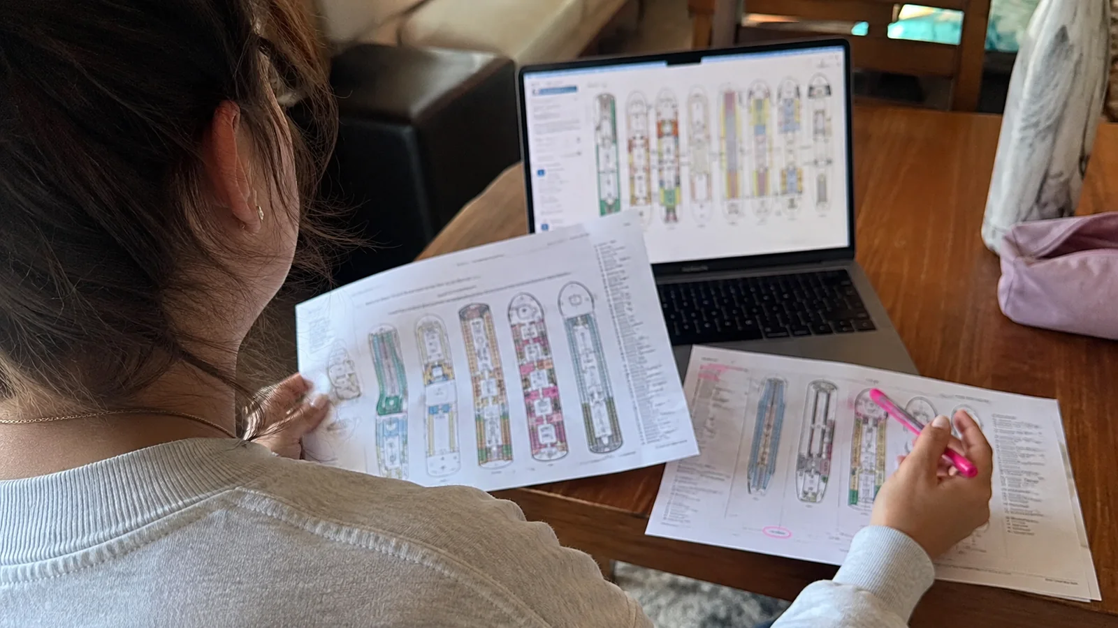 Woman highlighting printed cruise ship deck plans beside a laptop
