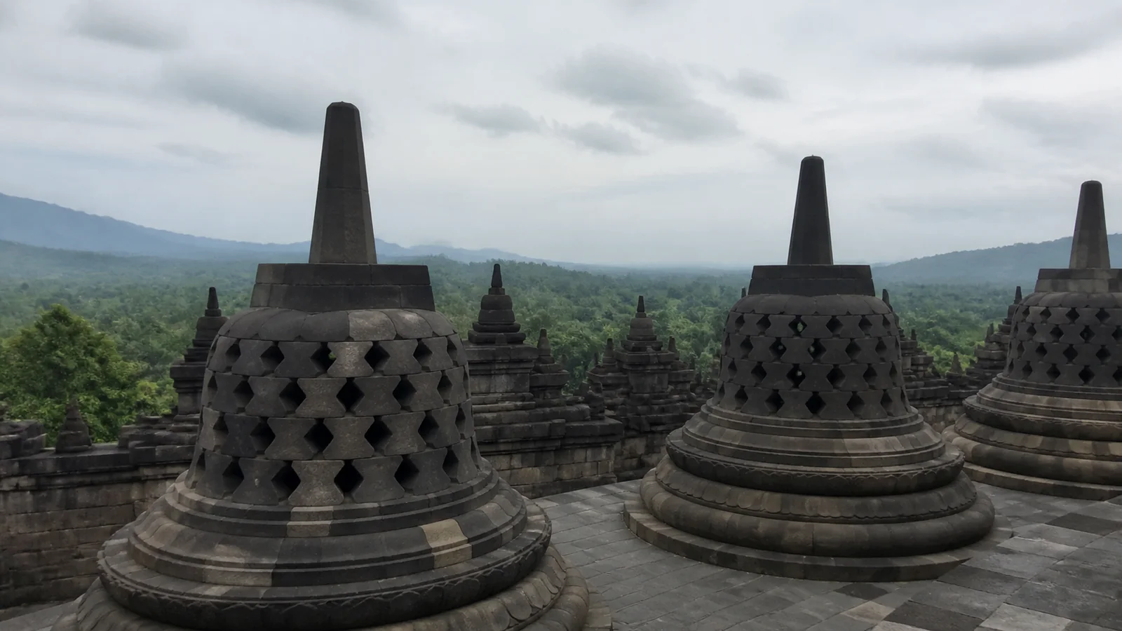 Bell-shaped stone stupas overlook a misty green landscape.