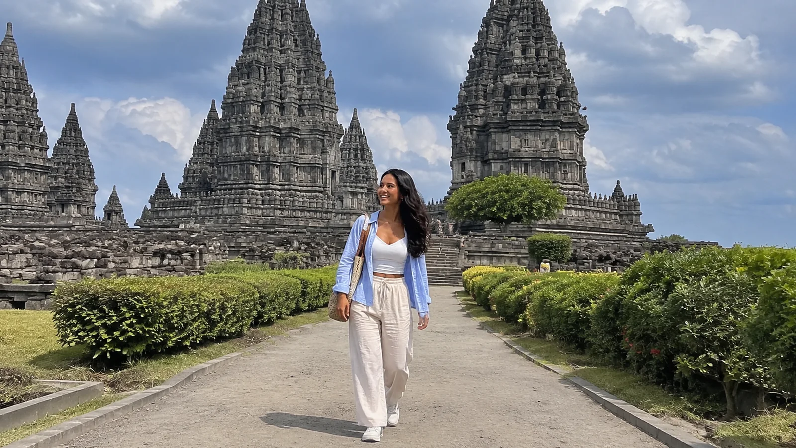 Woman walking between tall elaborately carved stone temple towers.