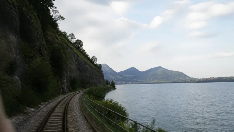 Railway track curving beside a lake beneath a steep green slope.