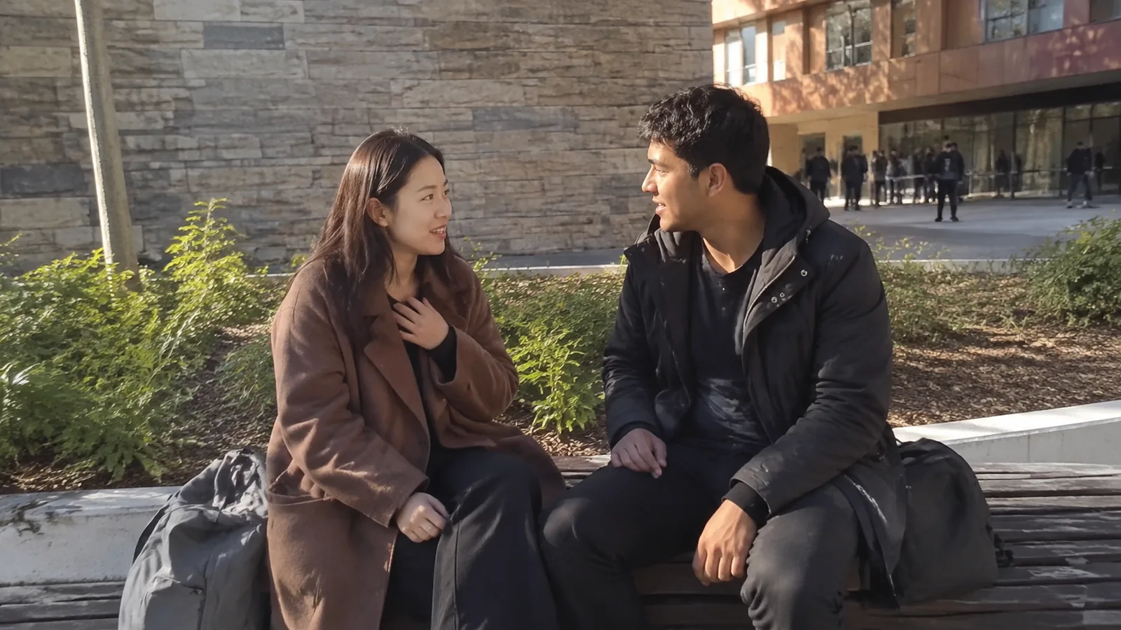 Two people talking while seated outside a stone building.