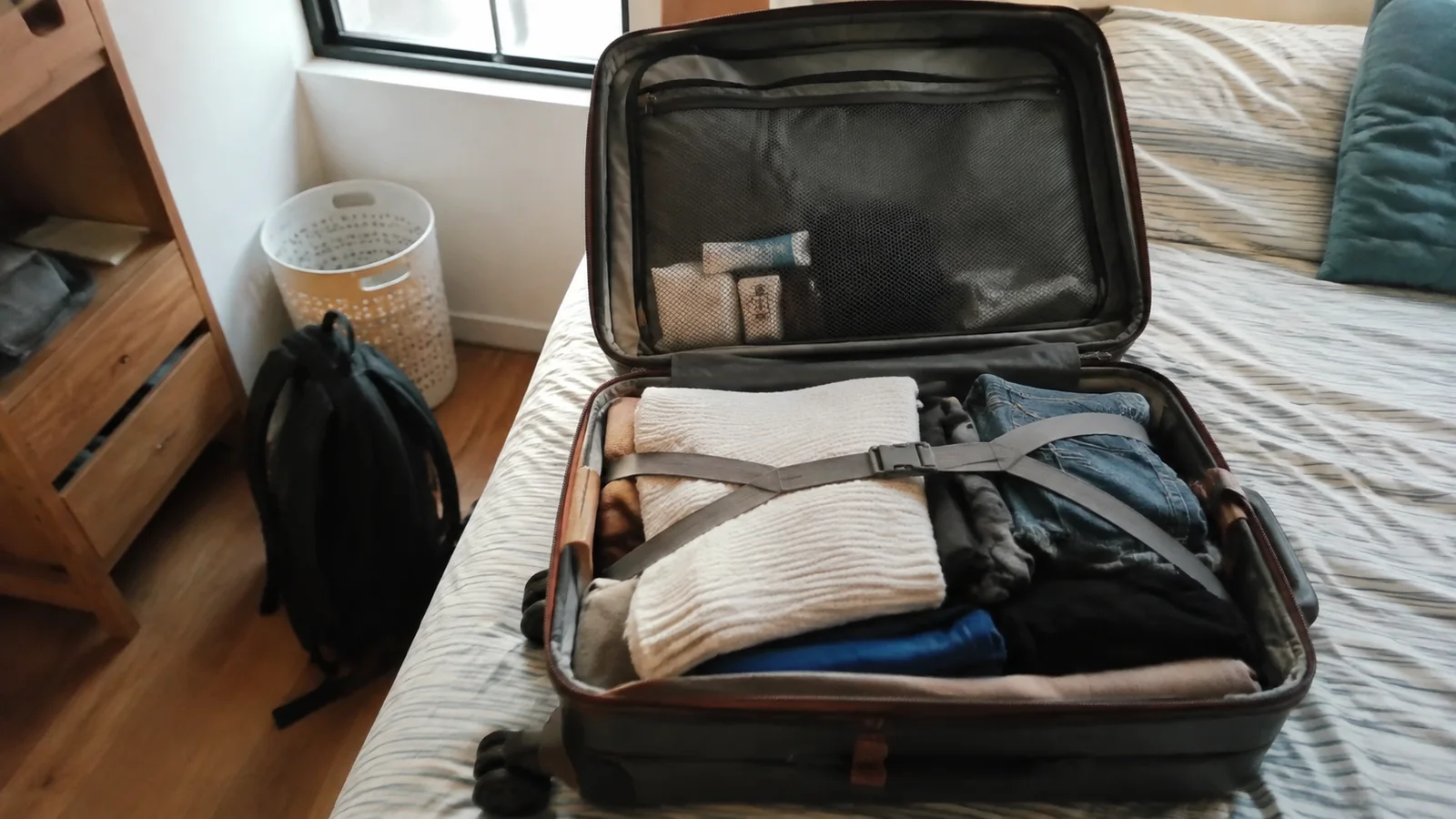 Open suitcase filled with folded clothing on a bed.