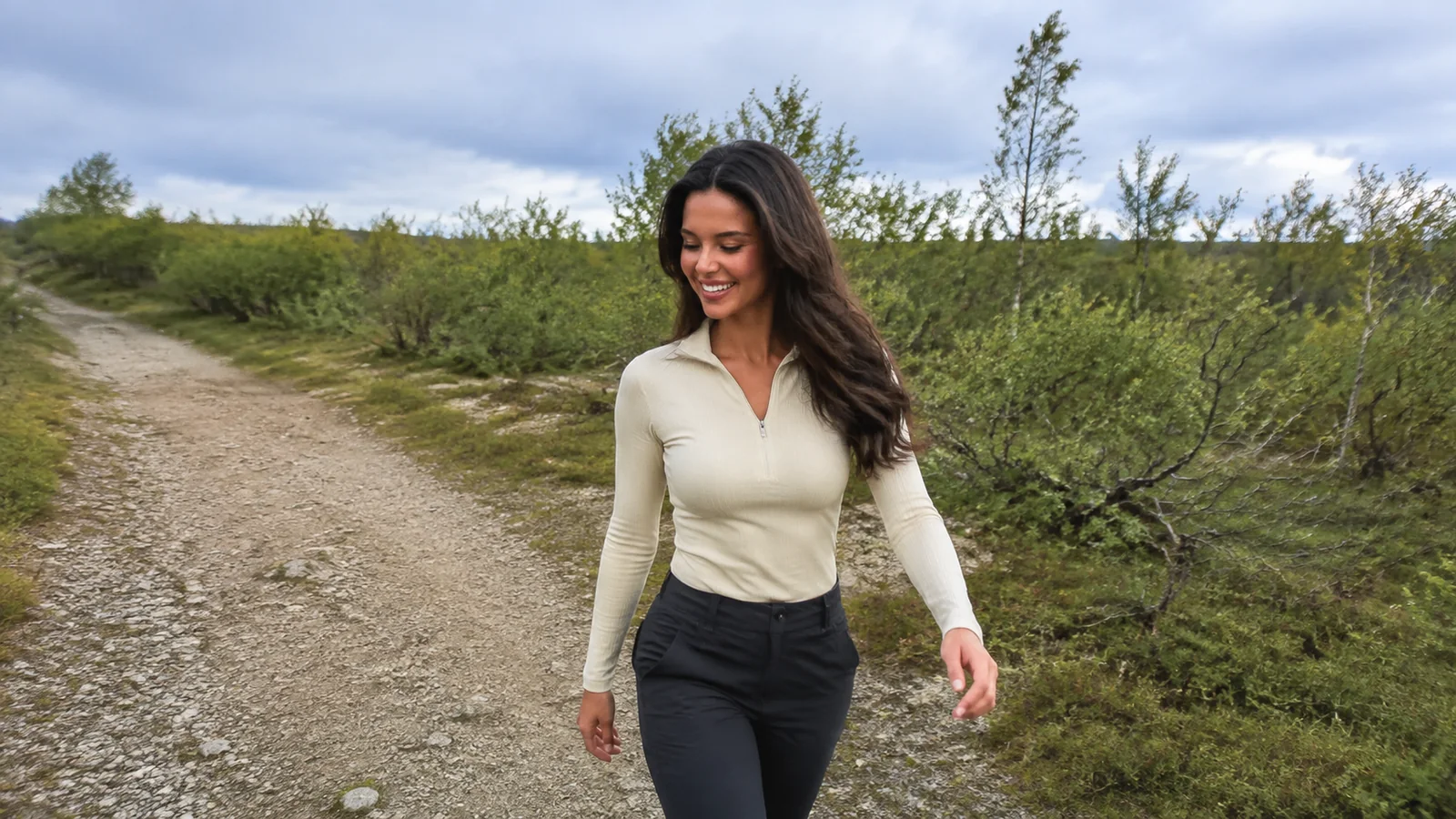 Woman walks along a gravel path through low shrubs.