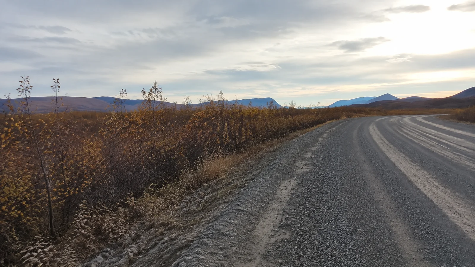 Gravel road curves through autumn scrub toward distant hills.