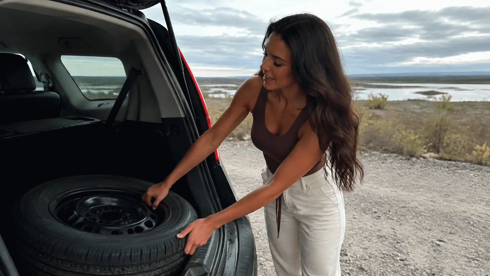Woman checks a spare tire in the open trunk of a vehicle.