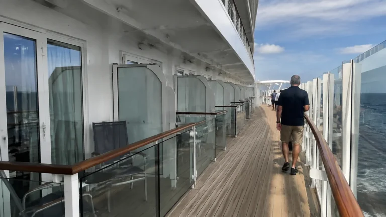 Passengers walking along a promenade directly outside cabin balconies.