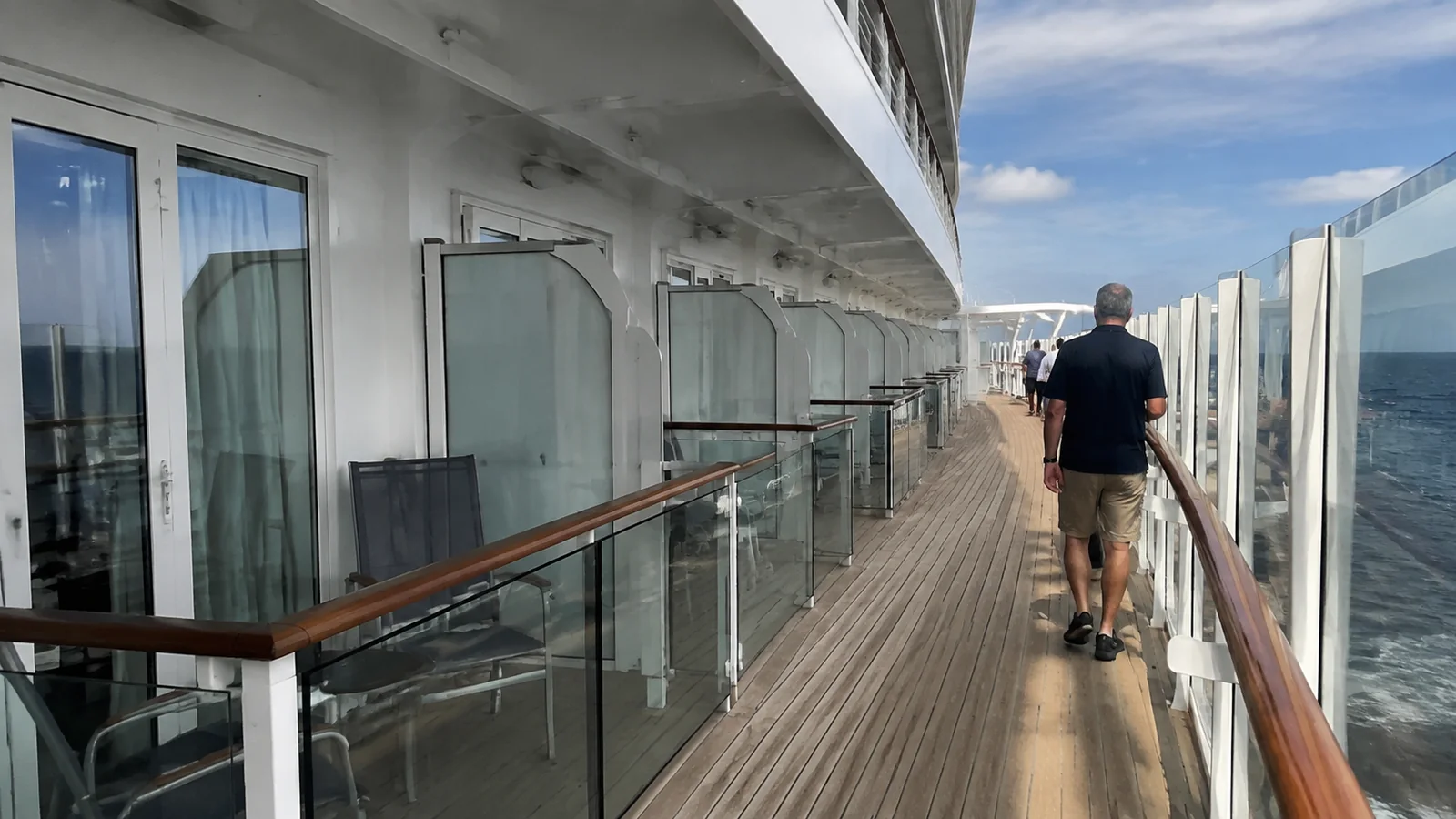 Passengers walking along a promenade directly outside cabin balconies.