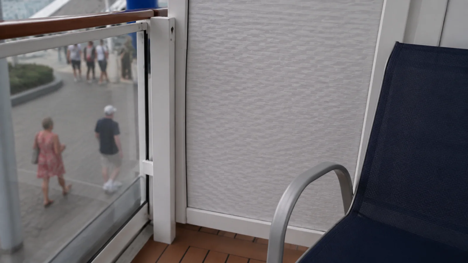Balcony chair beside a glass partition overlooking a public walkway.