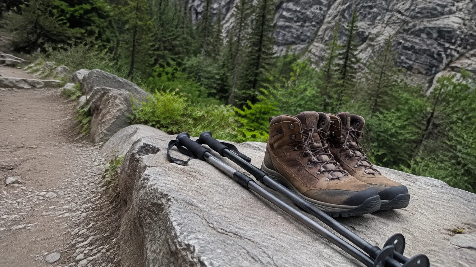 Hiking boots and trekking poles rest on a large trailside rock.