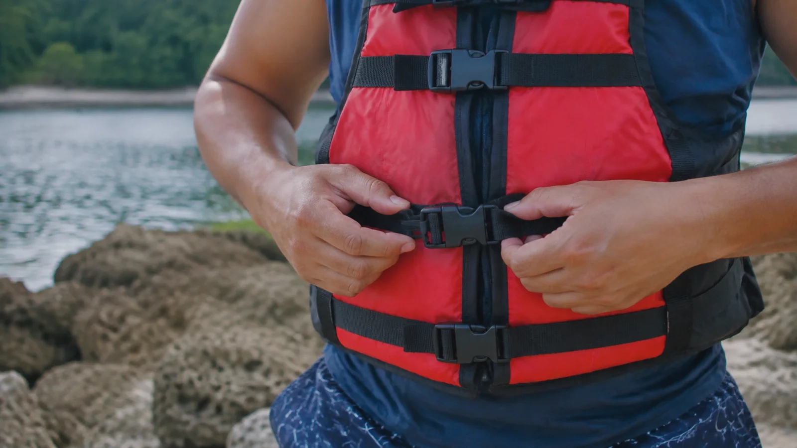 Hands fastening the waist buckle of a red life jacket.