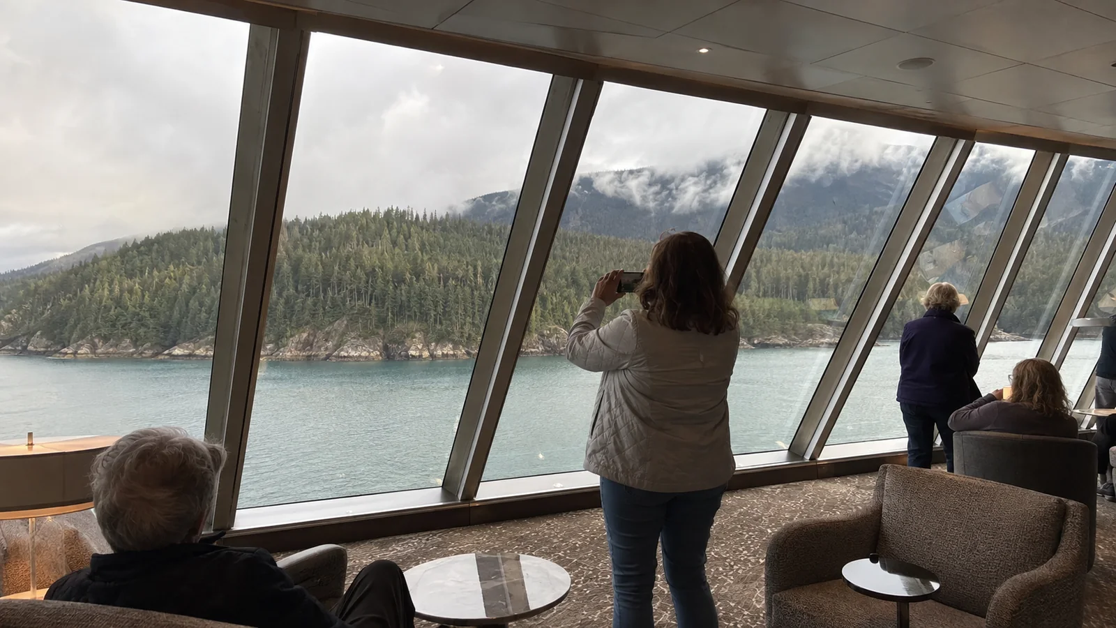 Passengers watching mountain scenery through a ship's observation-lounge windows.