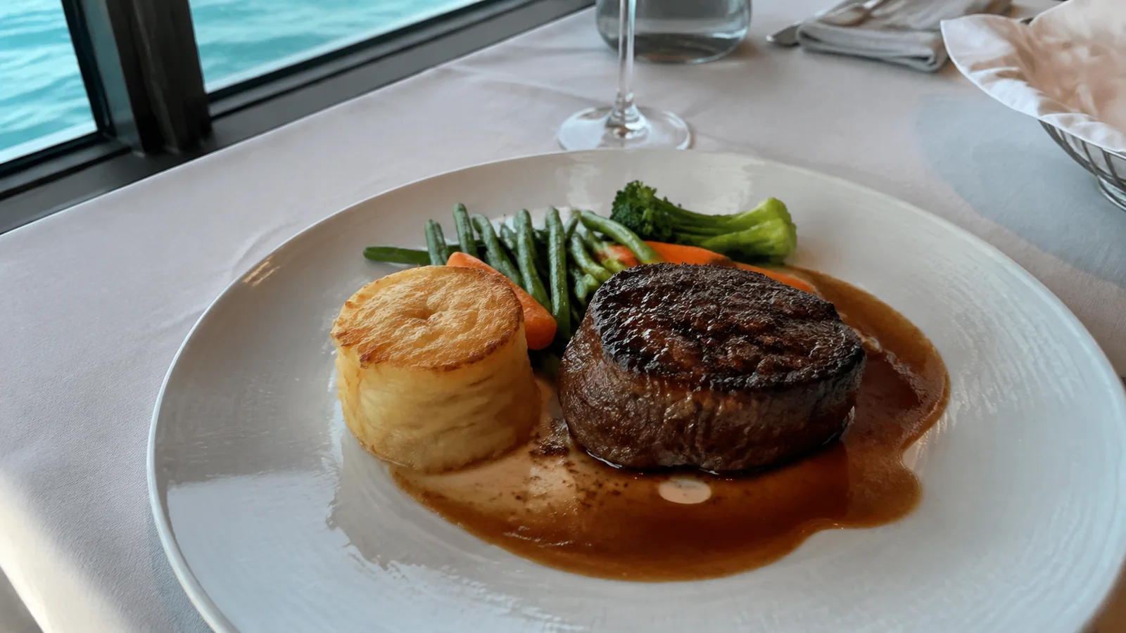 Steak, potato and green vegetables are served on a white plate.